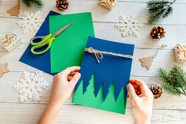 Concept de bricolage. Carte de vœux Joyeux Noël faite à la main avec sapin en papier coloré. Les mains du gamin tenant des objets artisanaux. Nouvelle année idée pour les enfants. Vue de dessus, plan plat - Photo, image
