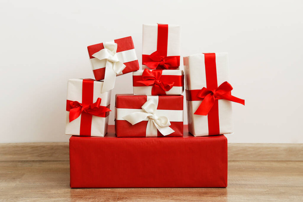 Christmas preparation concept. Stack of different colorful red and white presents for every family member. Pile of gifts in bright festive wrapping. Close up, copy space , white wall background. - Zdjęcie, obraz