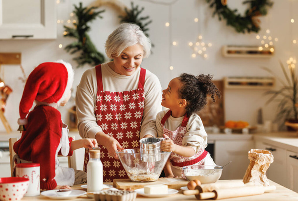 幸せな多人種の子供たちは、冬の休暇中に台所でクリスマスクッキーを調理する祖母を助ける - 写真・画像