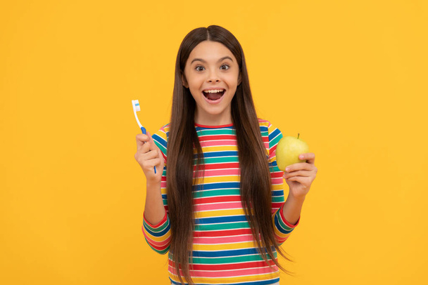 Beneficios sorprendentes de la higiene bucal. Chica sorprendida sostenga cepillo de dientes y manzana. Cuidado de los dientes - Foto, imagen
