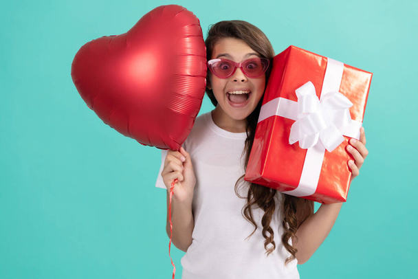 Güneş gözlüklü şık genç kız hediye kutusu ve kalp balonu tutuyor. Aşk hediyesi. Şaşırmış çocuk - Fotoğraf, Görsel