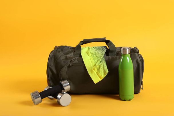 Sports bag and gym equipment on yellow background - 写真・画像