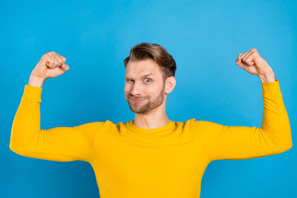 Photo of young guy happy positive smile show arms muscles bodybuilding isolated over blue color background - Fotografie, Obrázek