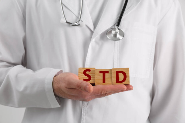 Doctor holding wooden cubes with abbreviation STD on white background, closeup - Valokuva, kuva