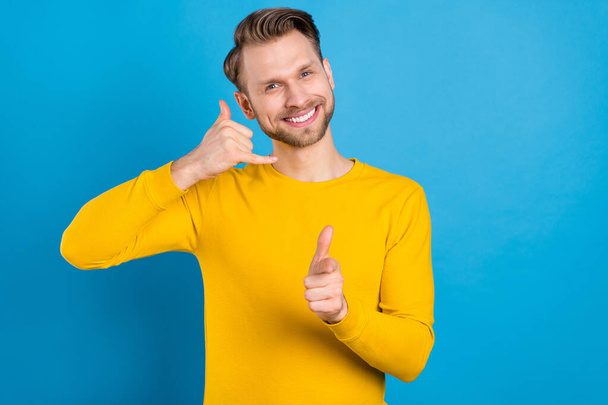 Photo of young man happy positive smile show call phone sign indicate finger you isolated over blue color background - Zdjęcie, obraz