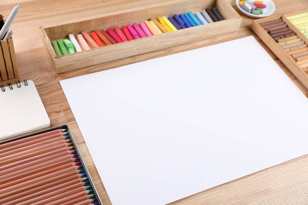 Blank paper, soft pastels and drawing pencils on wooden table at artist's workplace. Space for design - Foto, Imagem