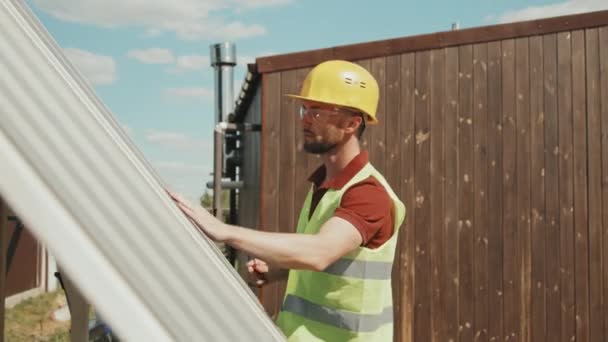 Tracking shot de ingeniero masculino en sombrero duro, gafas de seguridad y chaleco instalando paneles solares en el exterior - Imágenes, Vídeo
