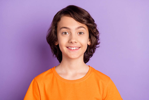 Portrait of attractive cheerful boy wearing orange t-shirt isolated over violet purple color background - Photo, Image