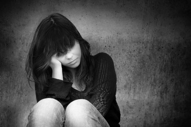 Black and white photo of a sad anonymous young woman who is thoughtful about troubles in front of a gray wall - Photo, Image