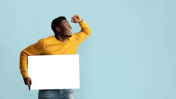 Zwarte man met lege reclamebord op zoek naar kopieerruimte - Foto, afbeelding