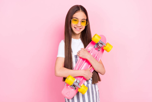 Photo of attractive sportive happy young girl hold hands hug longboard isolated on pastel pink color background - Foto, imagen
