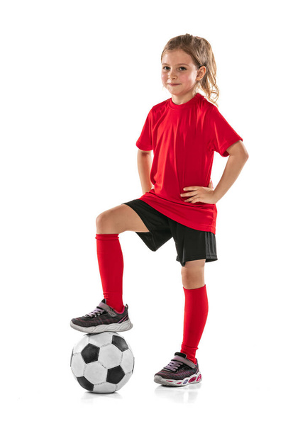 Full-length portrait of girl, child, football player in red uniform training, posing isolated over white background - Fotó, kép