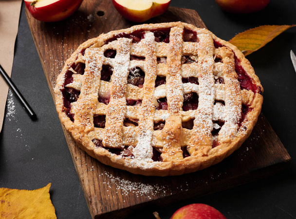 запечений круглий традиційний яблучний пиріг на коричневій дерев'яній дошці та свіжих червоних яблуках, вид зверху
 - Фото, зображення