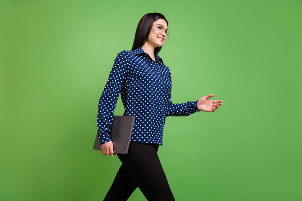 Profile photo of cute brunette hairdo business lady go give hand hold laptop wear spectacles blue shirt isolated on green color background - 写真・画像