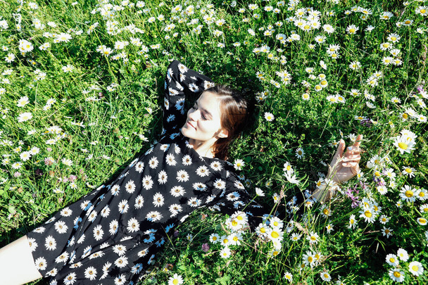 beautiful woman in a dress with flowers lies in the grass with daisies - Valokuva, kuva