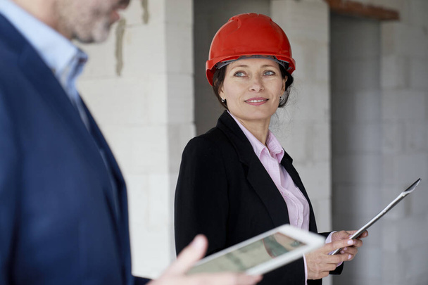 Ingeniera caucásica y mujer de negocios sosteniendo documento mientras está de pie en el sitio de construcción - Foto, imagen