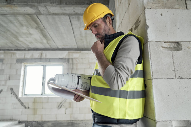 Caucasian engineer walking on construction site and browsing building plans - Fotó, kép