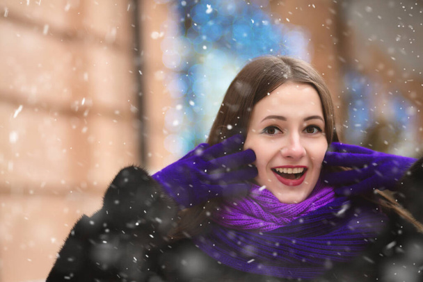 Mujer joven emocionada en traje de invierno caminando por la ciudad con copos de nieve - Foto, Imagen