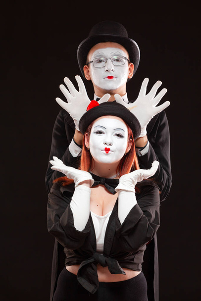 Portrait of two mime artists performing, isolated on black background. Man is standing behind the woman raising hands above her head. Fooling around - Zdjęcie, obraz
