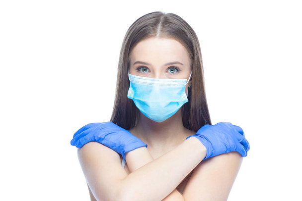 Studio shot on white background of a beautiful young woman wearing mask and latex gloves protected from coronavirus with her hands on naked shoulders stressed by quarantine - Foto, afbeelding