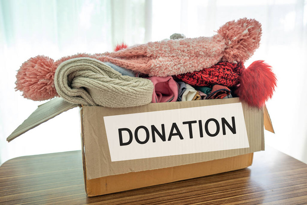 Тримання коробки для пожертвувань одягу з використанням одягу та ляльки вдома для підтримки допомоги бідним людям у світі
. - Фото, зображення