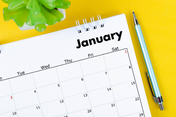 The January 2022 desk calendar and pen with plant pot on yellow background. - Photo, Image