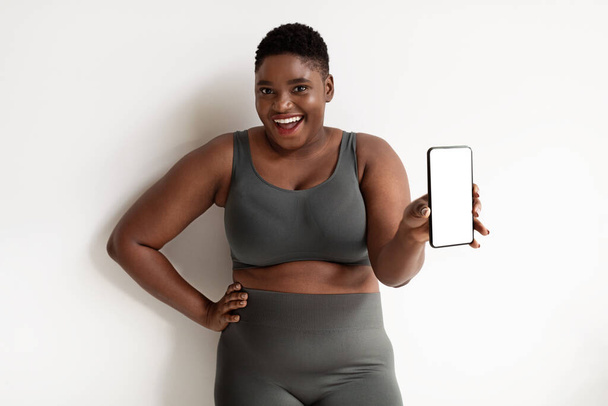 Smiling sporty african american plus size woman showing cellphone, mockup - Фото, изображение