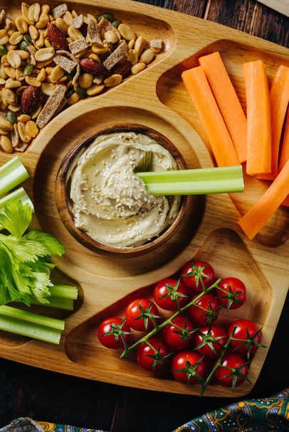 Hummus en groentesticks van wortel en selderij op een houten bord - Foto, afbeelding