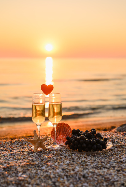 Romantyczne miejsce nad morzem. Słońce świeci nad wieczornym morzem nad kieliszkami szampana. Format pionowy, ostrość selektywna na szkle. - Zdjęcie, obraz