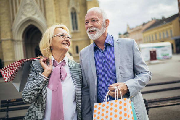 Güneşli bir günde alışverişleriyle yürüyen mutlu yaşlı çift. - Fotoğraf, Görsel