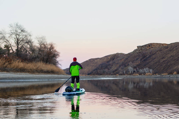 Un homme fait du rafting sur la rivière sur un plateau à la fin de l'automne dans la soirée, regardant au loin les montagnes. SUP - Photo, image