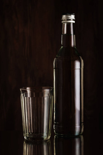 Faceted glass and a bottle of vodka on a dark background - Фото, изображение