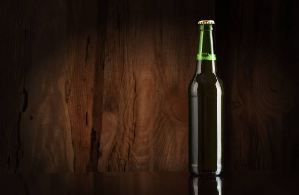 Green glass bottle with beer on the background of a wooden wall - 写真・画像