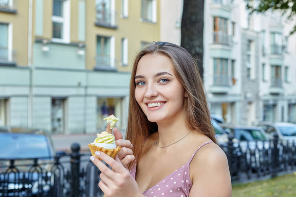 attractive girl with long hair holds a cake in her hands and spreads cream on her finger. photo shoot in the city. - Photo, image