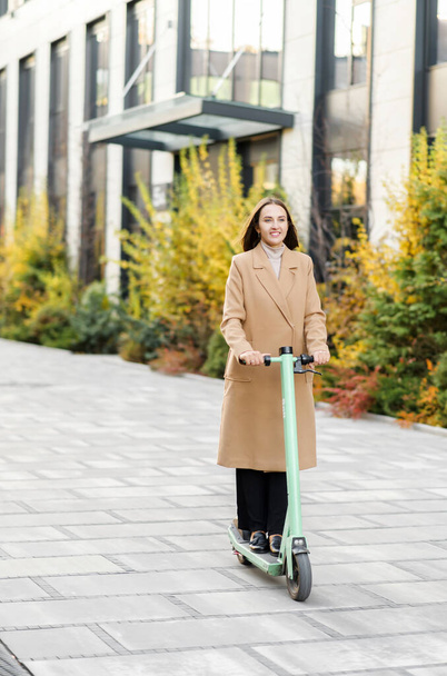 Ευτυχισμένη επιχειρηματίας ιππασία σε smart casual φορούν ιππασία στο γραφείο σε ένα e-scooter - Φωτογραφία, εικόνα