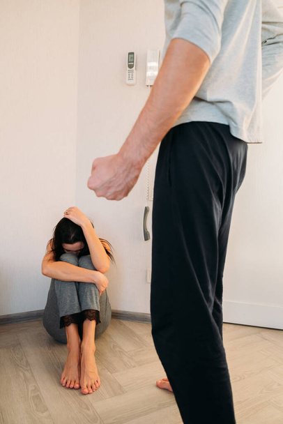 Huiselijk geweld. De man staat met zijn vuist voor zijn vrouw. Het meisje zit in een hoek van de kamer en huilt achter haar handen. Flarden telefoon hangt aan de muur. Proberen om hulp te roepen - Foto, afbeelding