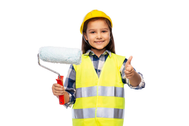 girl in helmet with paint roller showing thumbs up - Foto, afbeelding