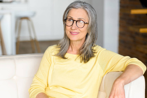 Close-up portrait of contemporary senior woman wearing stylish eyewear looks at the camera and smiles - Foto, imagen
