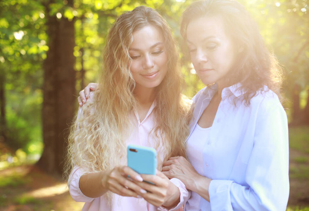 Portrait of Adult caucasian daughter showing on mobile phone to her senior mother outdoor - Fotó, kép