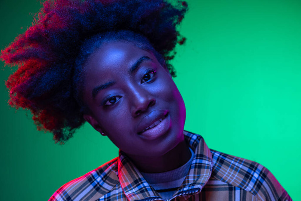 Close-up African young girls portrait on dark green studio background in purple neon light. Afro hairdo. Concept of human emotions - Valokuva, kuva