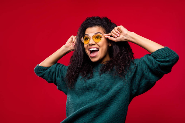 Photo of cute impressed dark skin lady wear green sweater arms eyewear looking empty space smiling isolated red color background - Fotografie, Obrázek