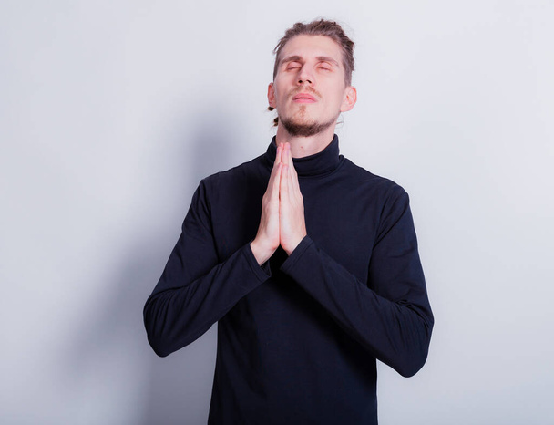 Man praying or ask apologizes with hands closed. Man in dark gray turtleneck and short dreadlocks on head grey background copy space - Foto, Imagem