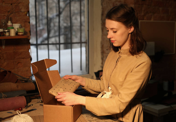 Young woman folds packing box in sewing workshop - Foto, afbeelding