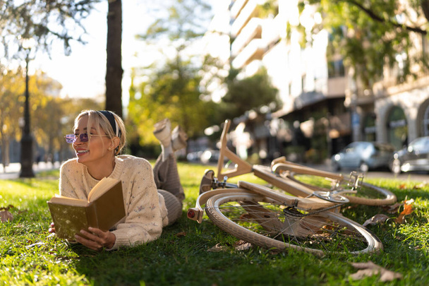 Mosolygó nő feküdt közel kerékpár és az olvasás könyv - Fotó, kép