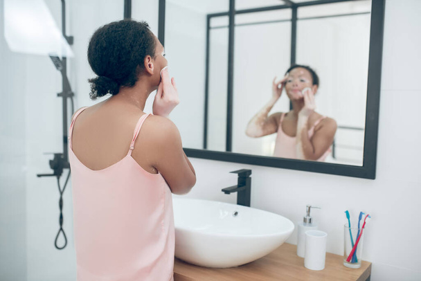 A woman in pink lingerie in a bathroom while doing beauty procedures - Foto, Imagen