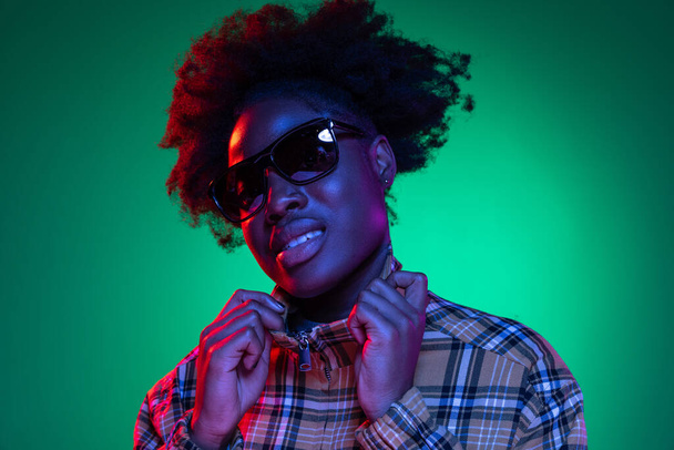 Close-up African young girls portrait on dark green studio background in purple neon light. Afro hairdo. Concept of human emotions - Foto, Bild