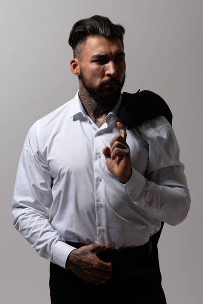 Vousatý hispánec v tmavé vestě a bílé košili s kravatou při pohledu na kameru s rukama v kapsách ve studiu - Fotografie, Obrázek