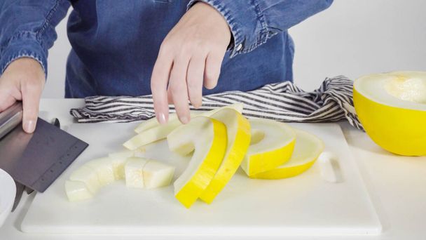 Step by step. Slicong golden dewlicious melon on a white cutting board. - Fotó, kép