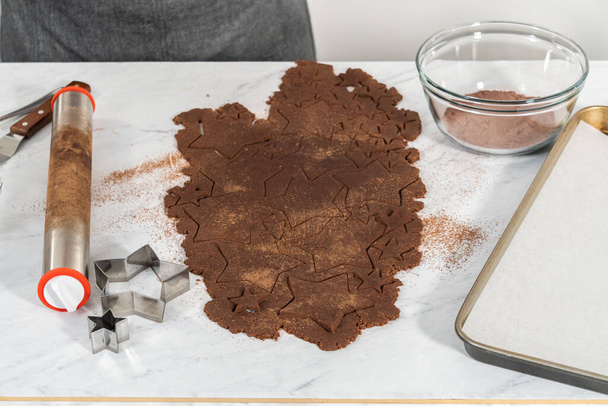 Вырезание шоколадных крекеров в форме звезды из теста с помощью резака для печенья. - Фото, изображение