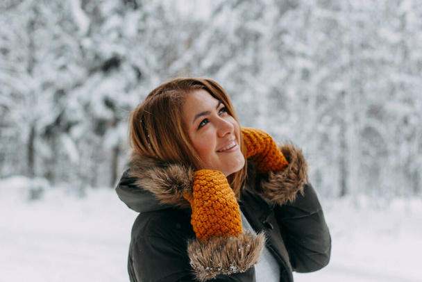 Portrait of a happy girl with a short haircut in mustard mittens in the forest after a snowfall . Christmas holidays, outdoor activities. - Photo, Image